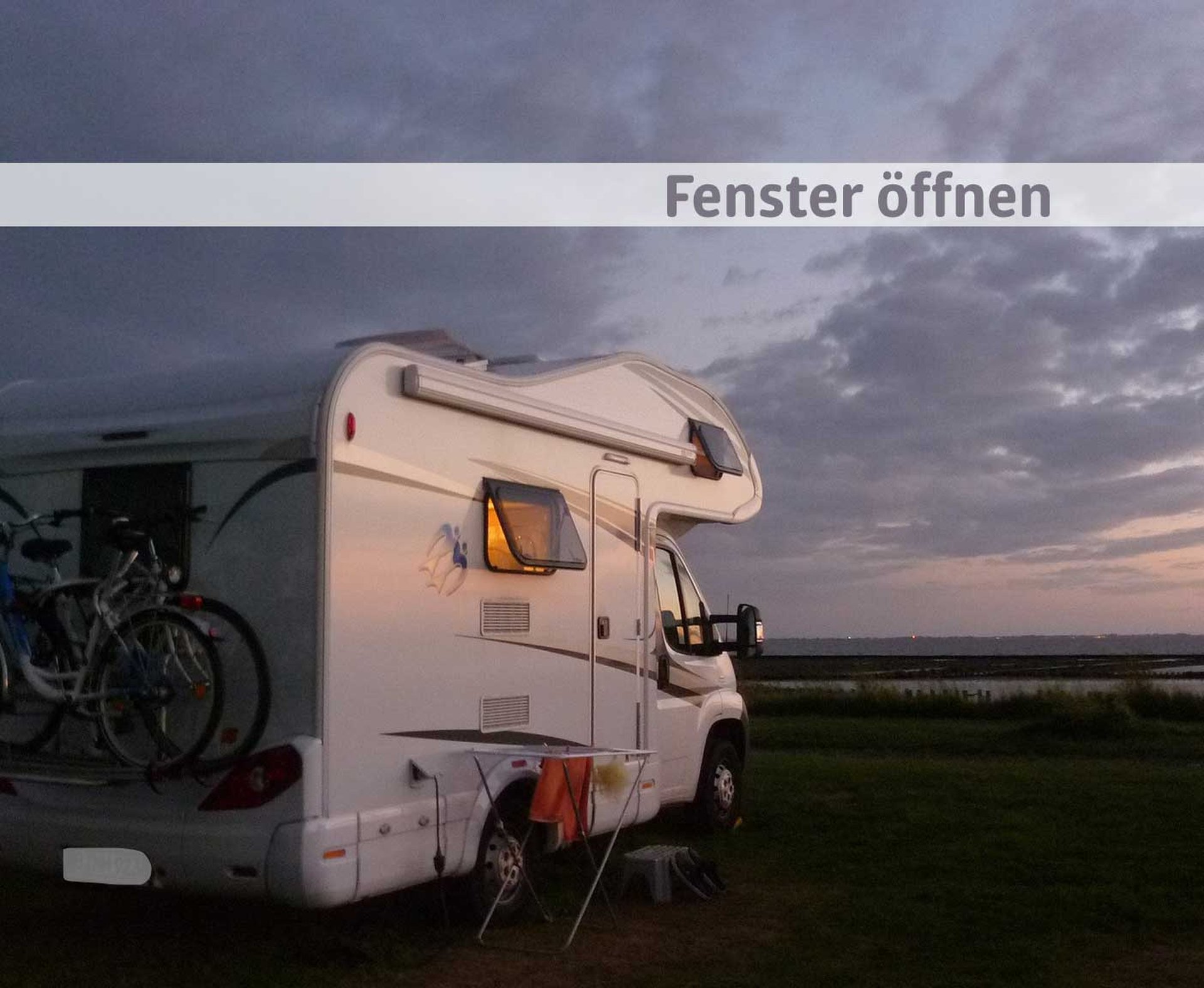Wohnmobil mit geöffnetem Fenster vor Meer und dunkelblauem Himmel nach dem Sonnenuntergang