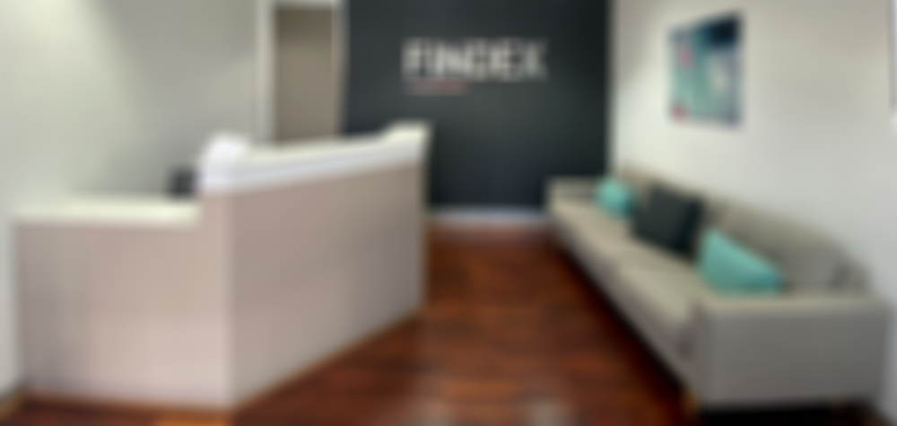 Findex Lismore office reception area, with a grey modern couch with 3 blue pillows, facing a reception desk, the Findex logo is on a dark wall at the back of the room.