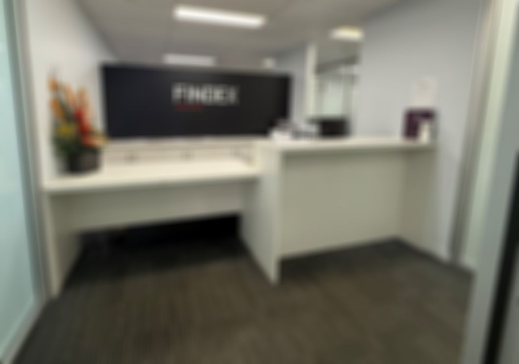 Findex Innisfail office reception area with "FINDEX" on a black wall, a desk, flowers on the counter, and grey carpet flooring.