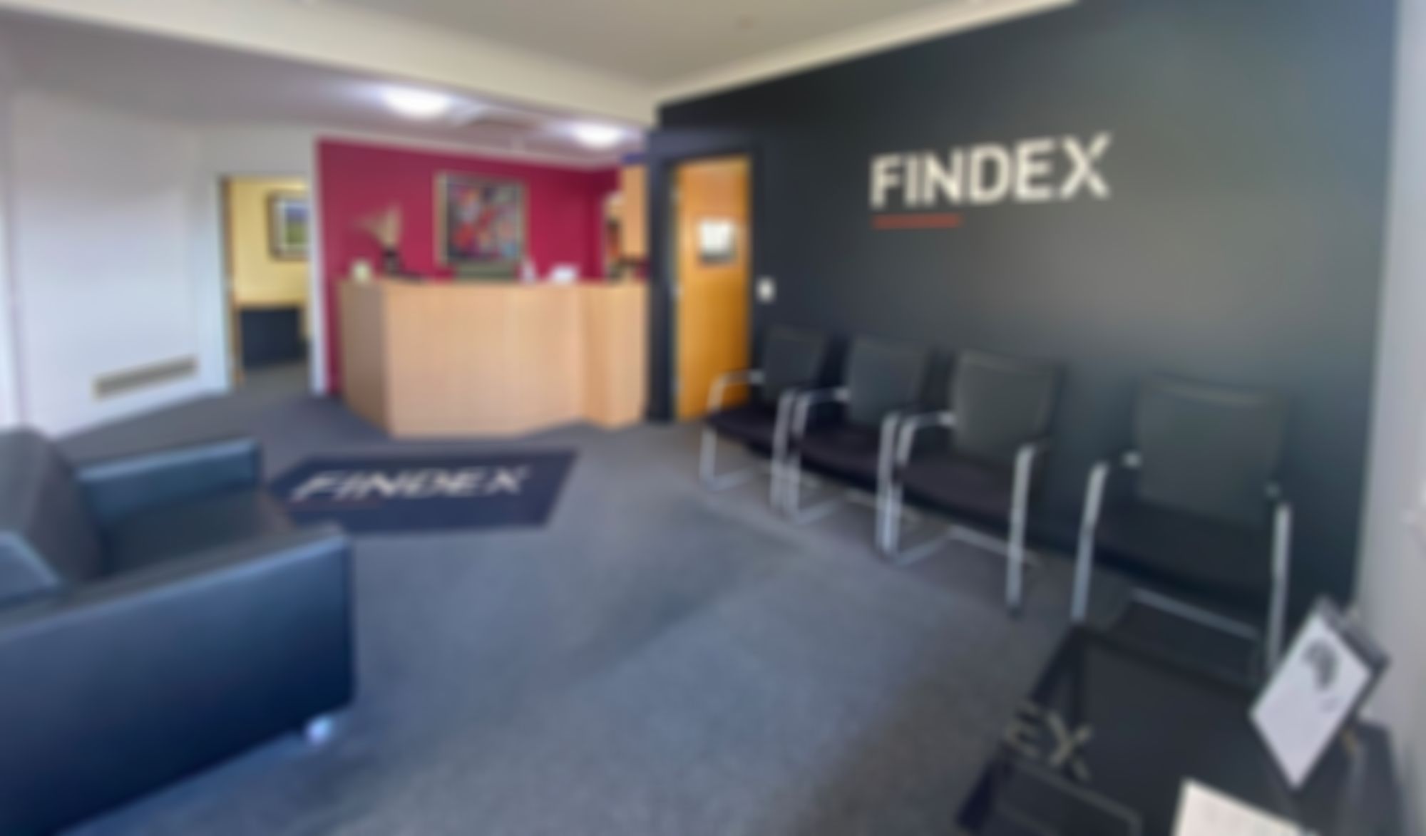 Findex Glen Innes Office lobby with black walls featuring the "FINDEX" logo, black chairs, a black couch, and a wooden reception desk with a red accent wall.
