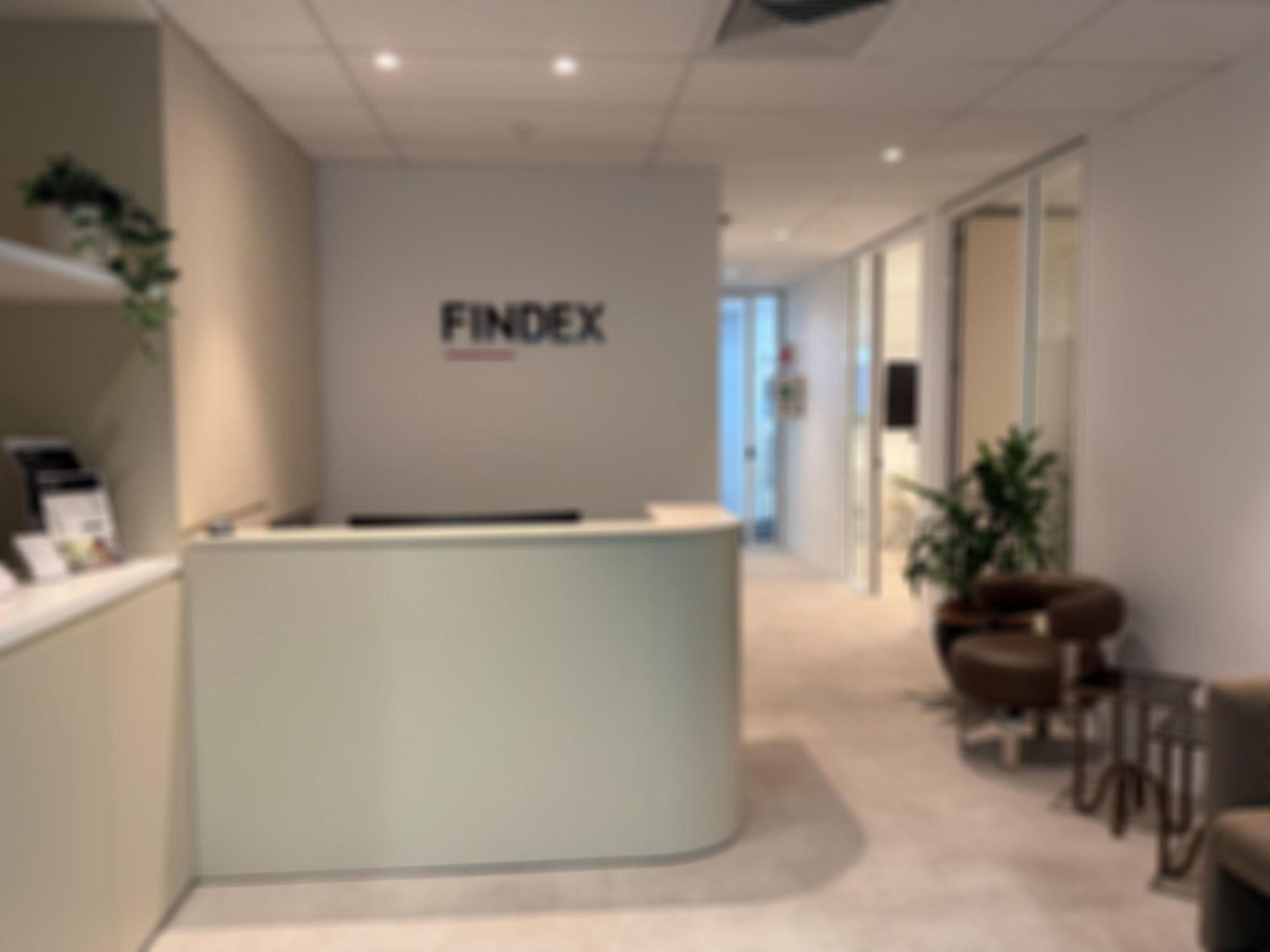 Findex Coffs Harbour office reception with the Findex logo on the wall. A reception desk, seating area, plants, and glass-walled rooms are visible in a modern setting.