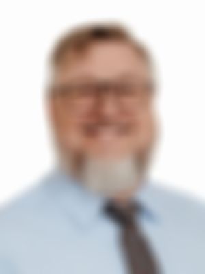 Ian Krarup is smiling with glasses, a beard, wearing a light blue shirt and patterned tie, against a white background.