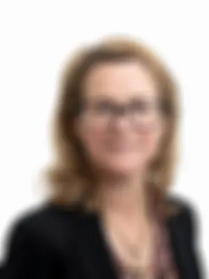 Tanie Green wearing a black blazer and floral blouse, smiles at the camera against a white background.
