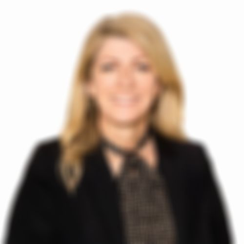 Kath Nell smiling with long blonde hair, wearing a black blazer and a patterned scarf, against a plain white background.