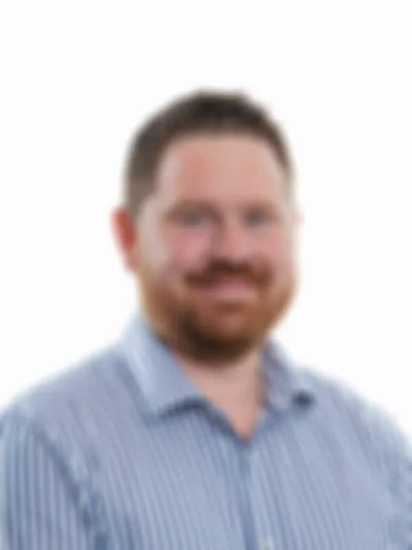 A man with short hair and a beard wearing a blue and white striped shirt smiles at the camera against a plain white background.