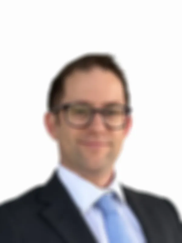 Man in a suit and tie, wearing glasses, smiling, against a plain white background.
