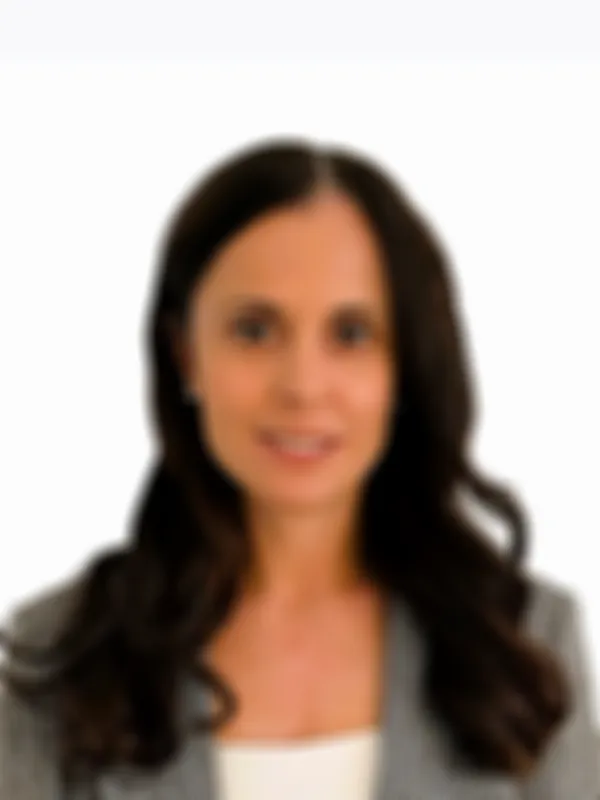 Natalie Frasca wearing pearl earrings and a checkered blazer. She is smiling and standing against a plain white background.