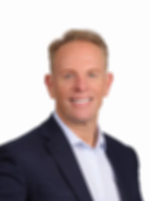 Andrew Reid in a dark suit and light dress shirt smiling against a plain white background.