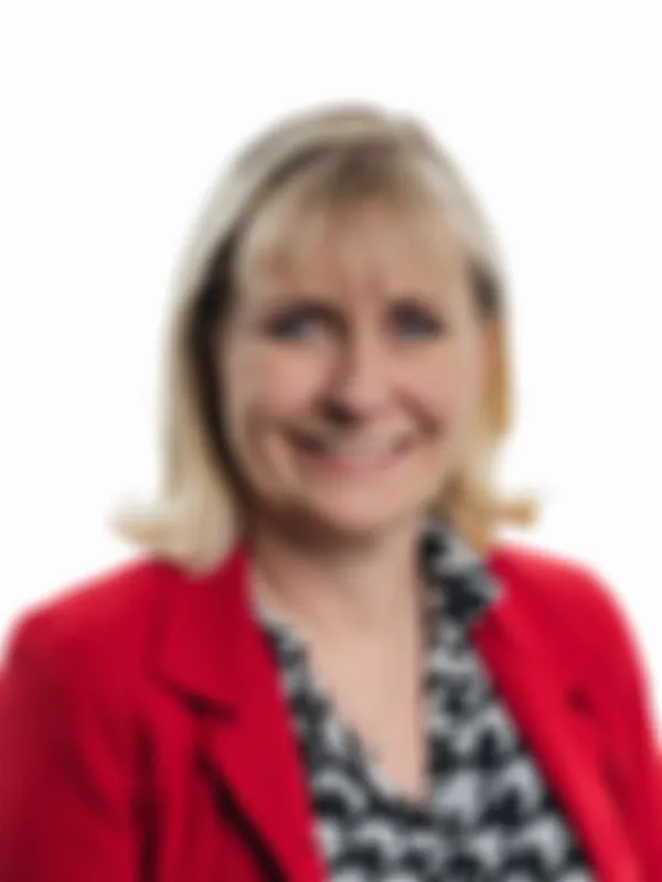 Smiling woman with short blonde hair, wearing a red blazer and a patterned shirt, against a white background.
