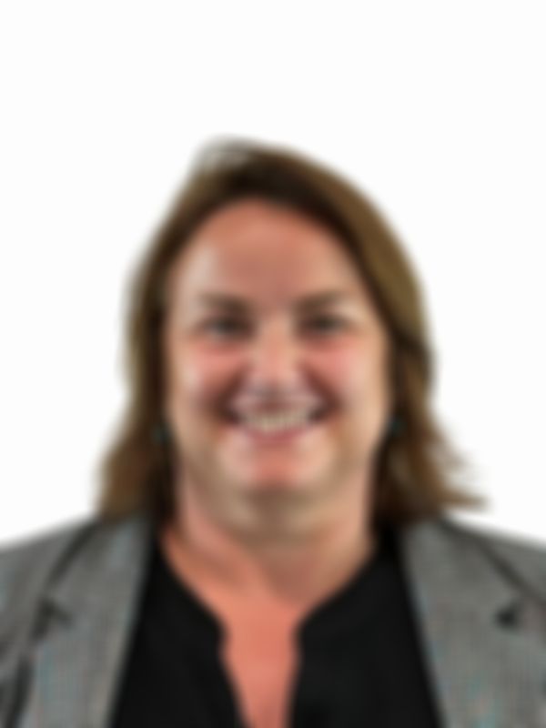 Smiling woman with brown hair wearing a grey blazer and black top against a plain white background.