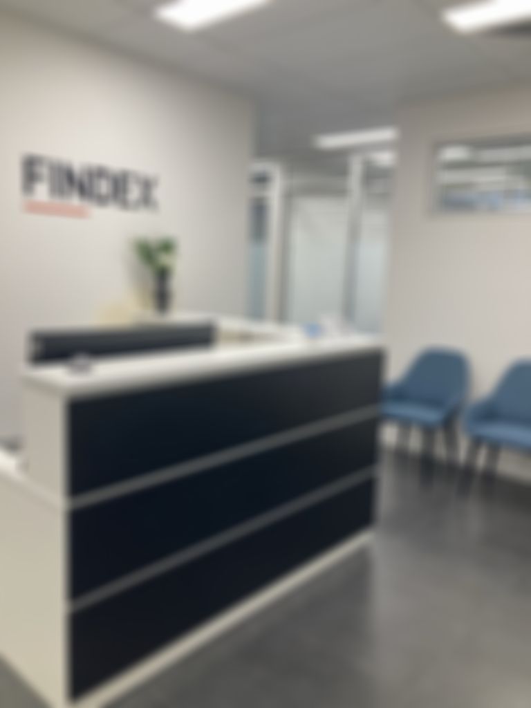 Modern office reception with a black and white desk, "FINDEX" logo on the wall, two blue chairs, and a small plant.