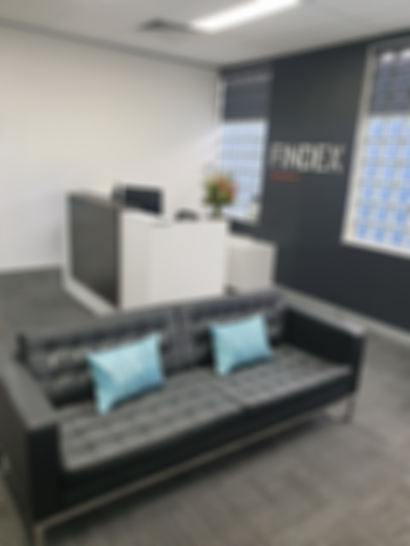 Modern office lobby with a black leather sofa, blue pillows, a reception desk, and the word "FINDEX" on the wall. Large windows in the background.