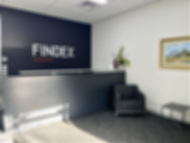 Hamilton office reception area with a dark desk, "FINDEX" on the wall, a grey chair, small table, and a framed landscape painting.