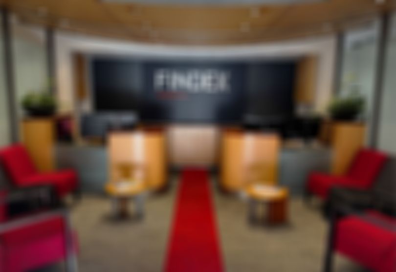 Modern reception area with a "FINDEX" sign, wooden desks, red chairs, a red carpet, and potted plants on each side.