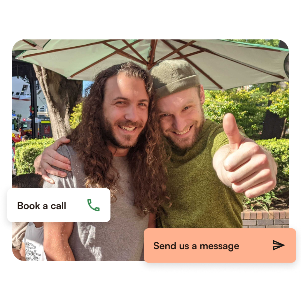 Two Humanitix staff, Jake and Sam, are pictured hugging and similar to the camera. Jake is on the left, and Sam is on the right, giving a thumbs up to the camera. Super imposed are two website interface buttons on the left and bottom right corners of the screen. They read "Book a Call", and "Send us a message".