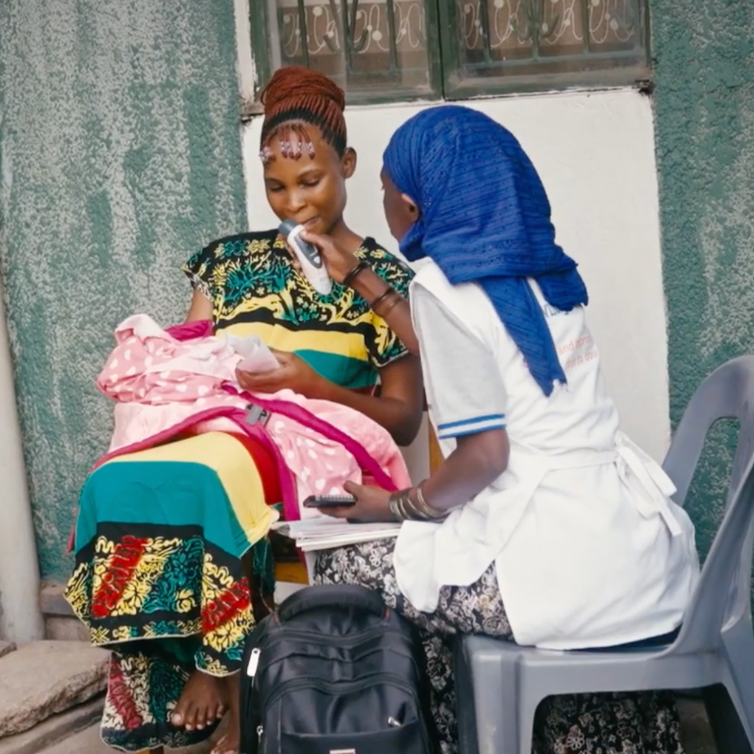 Woman holding newborn baby being checked over by a healthcare worked in a blue headscarf