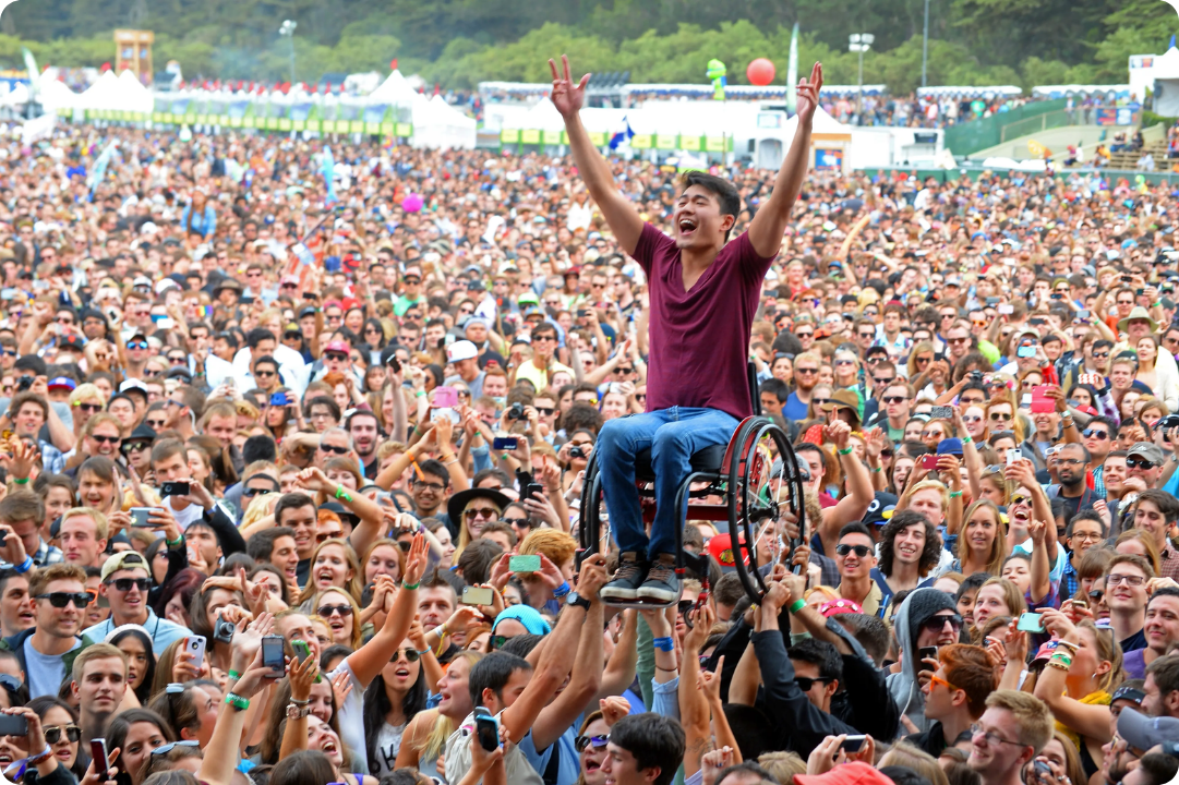 A patron at a music festival in a wheelchair being lifted by the crowd