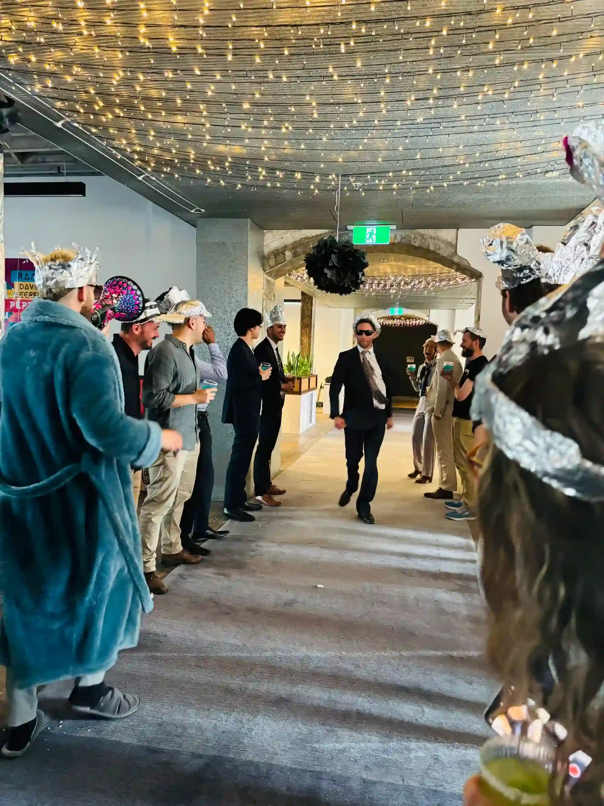 Josh walking down the office hallway in a tin foil hat surrounded by staff with tin foil hats on Impact Day 2023