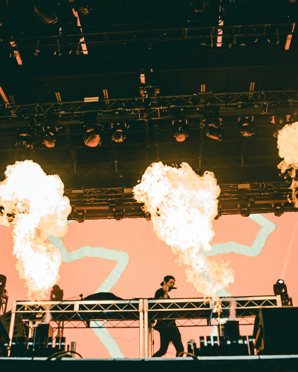 A festival stage with a DJ and fire balls