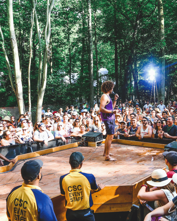 A speaker in the middle of a stage in a forest surrounded by the audience