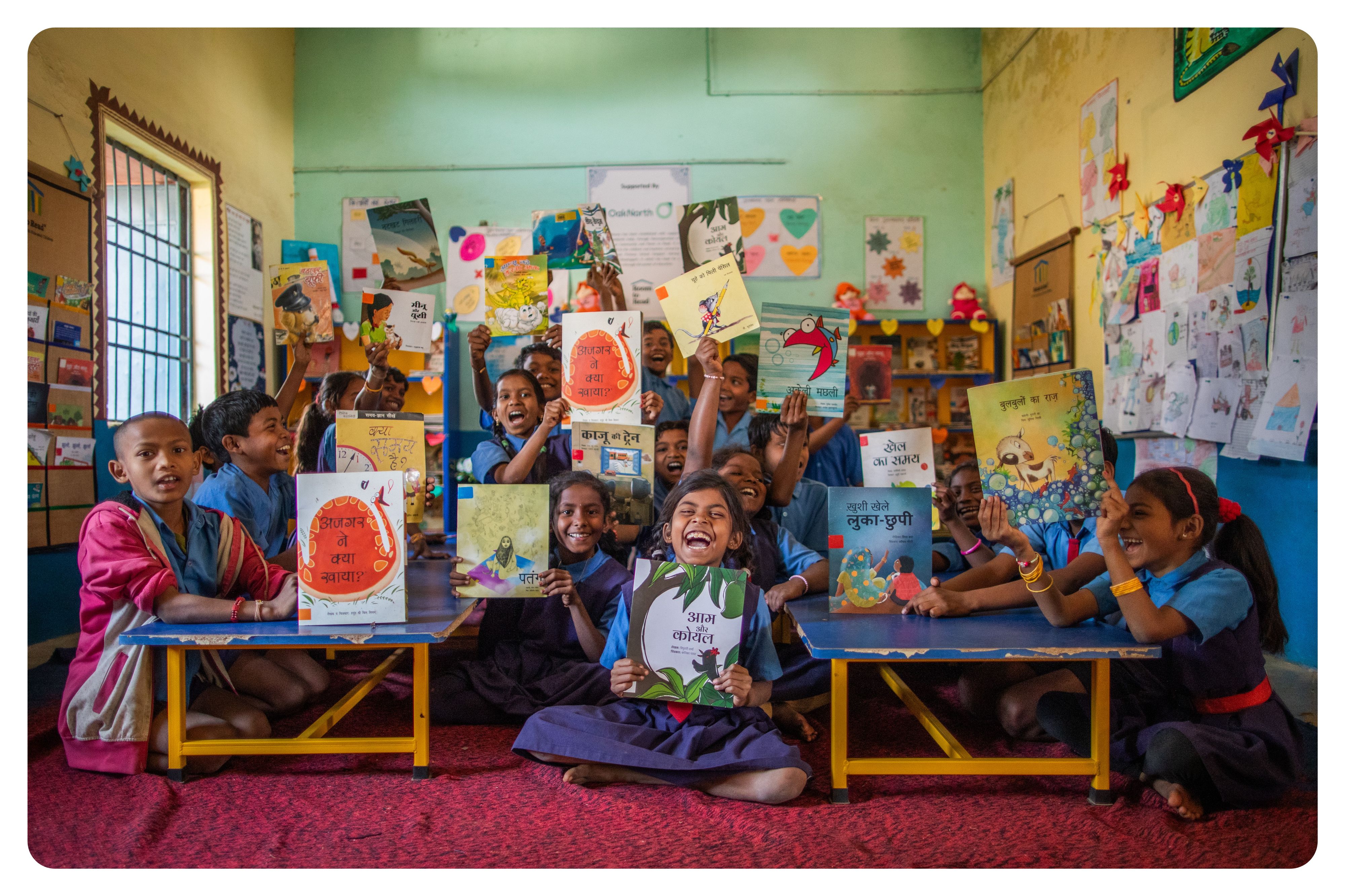 Smiling kids holding up picture books in a colourful classroom