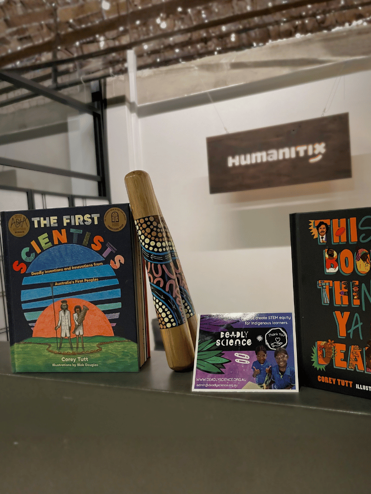 Books, card and clapsticks from DeadlyScience in front of Humanitix sign