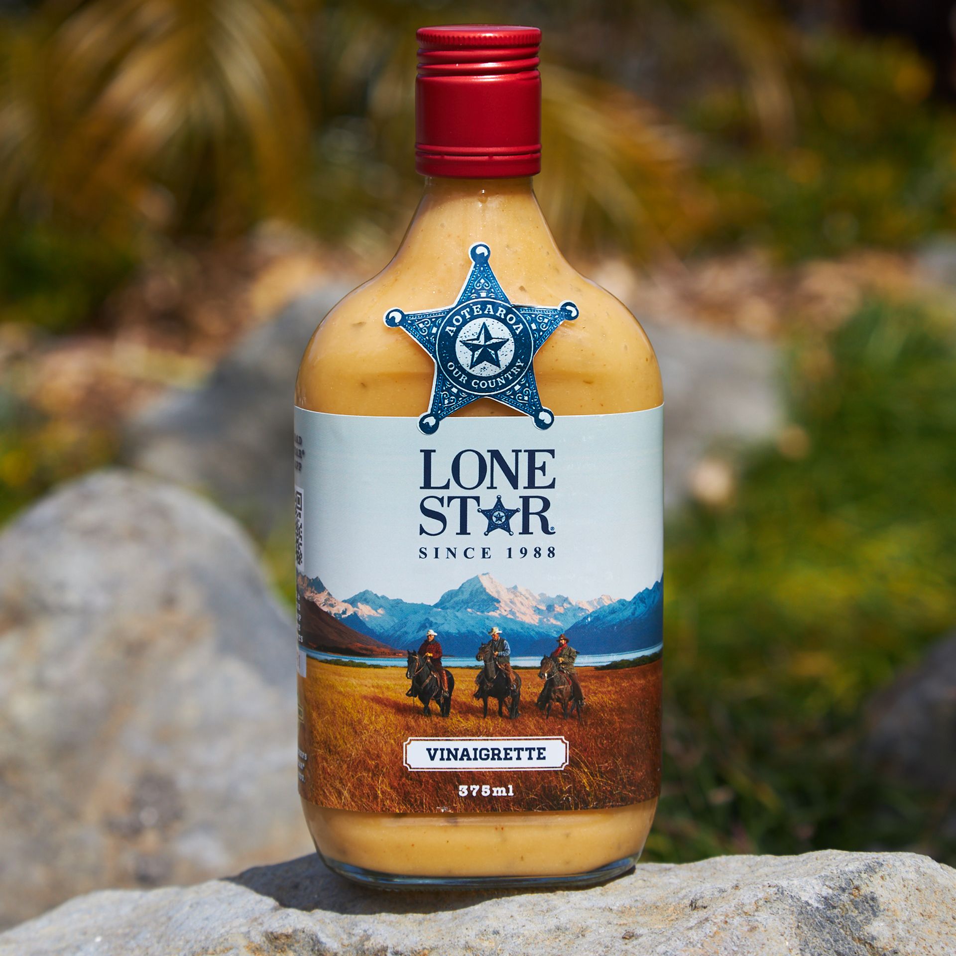 Bottle of Lone Star vinaigrette with a Western-themed label, featuring cowboys on horseback, set outdoors on a rock.