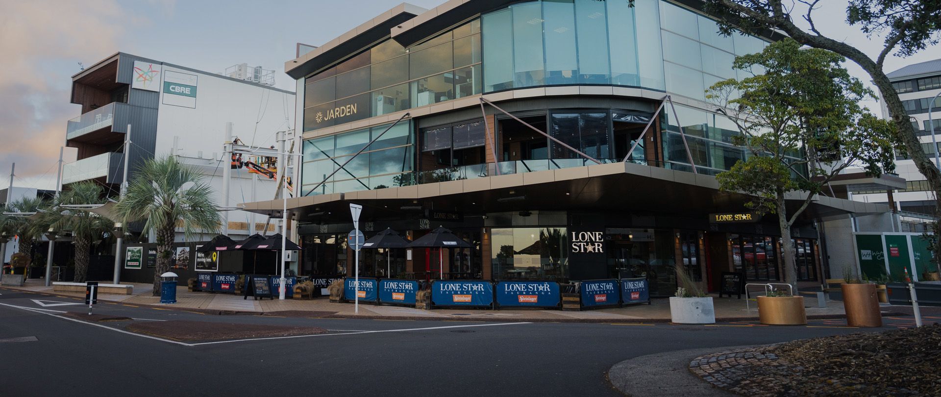 Street view of a modern corner building with glass windows, housing a restaurant named "Lone Star," outdoor seating, and surrounding greenery.