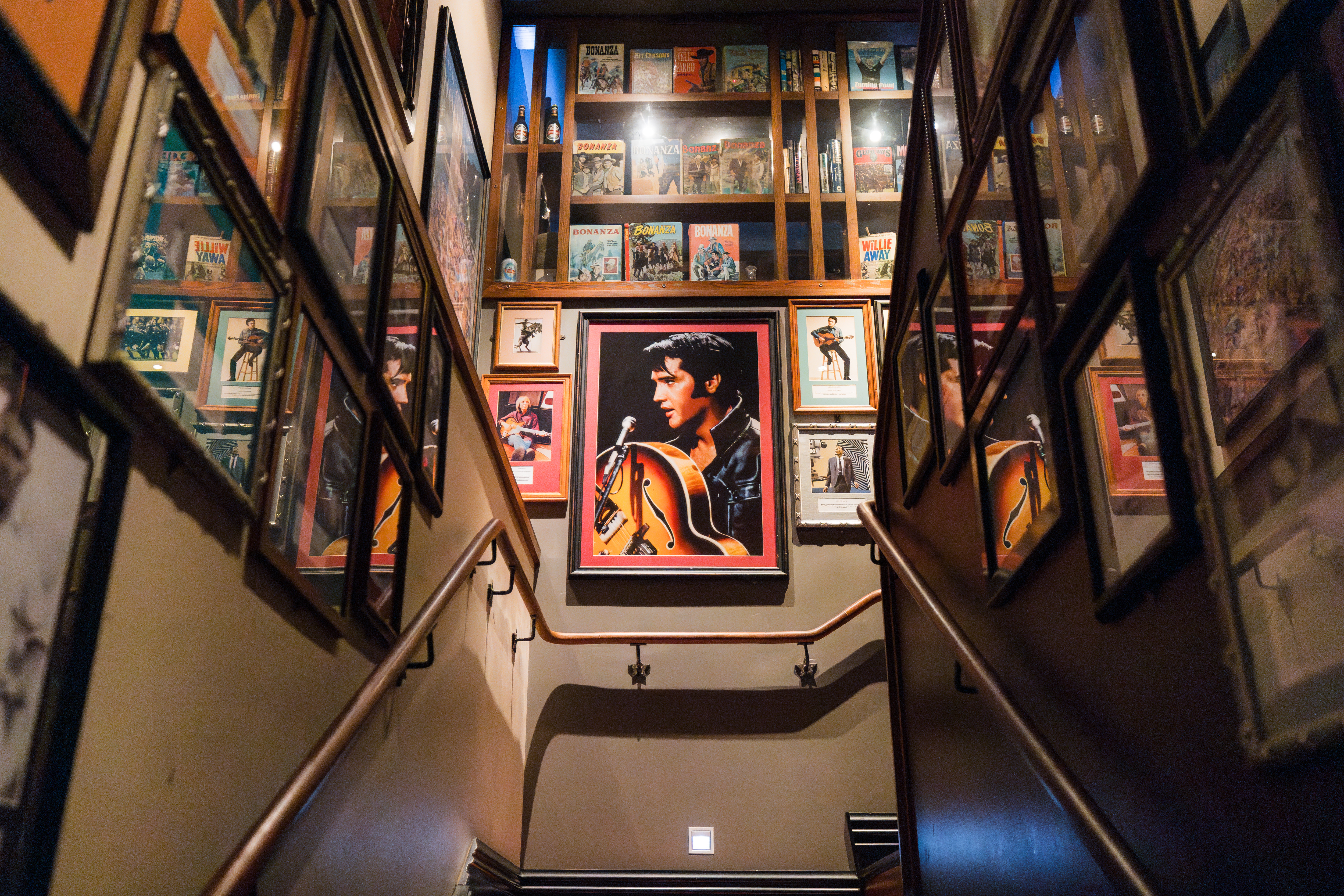 A staircase lined with framed posters and photos, featuring a large central portrait of a musician holding a guitar.