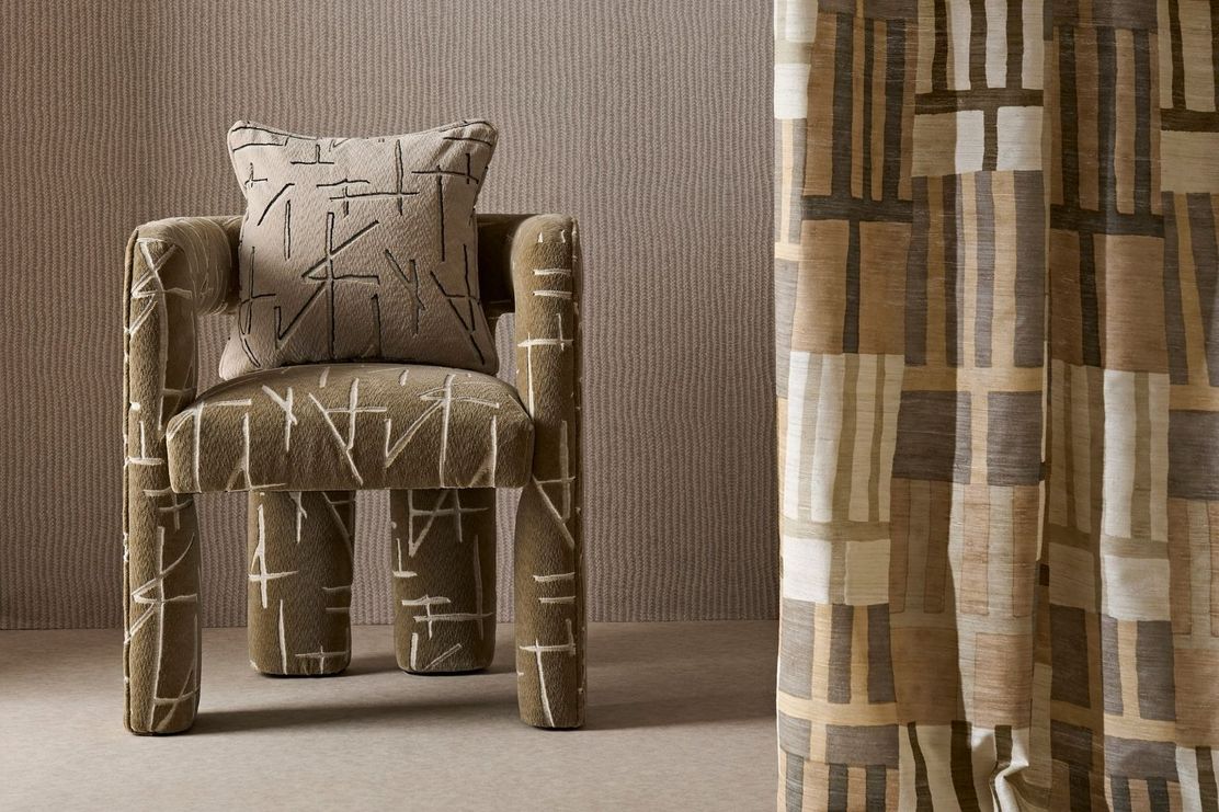 A modern armchair with abstract patterns and a matching pillow beside a curtain with geometric designs in neutral tones.