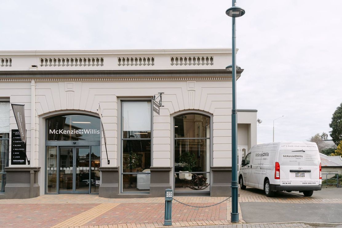 Street view of a McKenzie & Willis store with large windows, a parked company van.