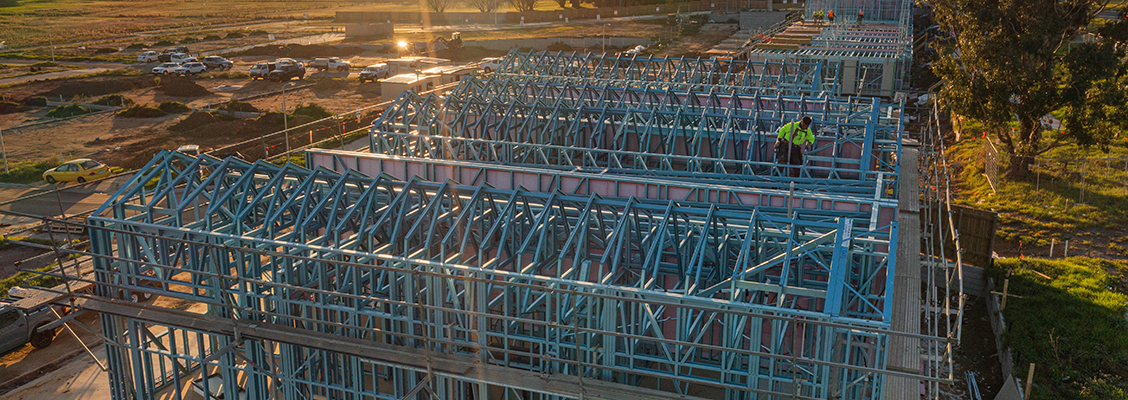 Aerial view of a construction site with TRUECORE steel framed homes and workers in safety gear, surrounded by open land and parked vehicles.