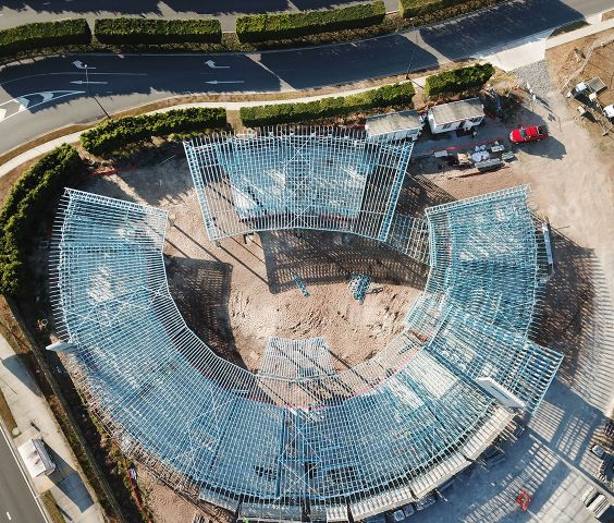 Aerial view of a curved childcare centre under construction, showcasing frames made from blue TRUECORE steel a dirt lot, surrounded by roads and greenery.