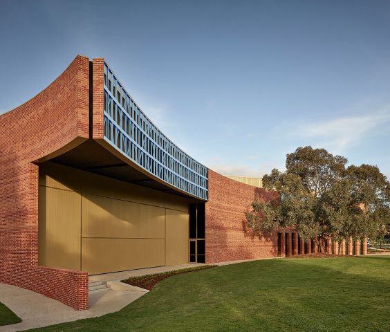 Curved brick building, the facade is supported by light gauge steel framing made from blue TRUECORE steel. It's surrounded by green grass and trees under a clear sky.
