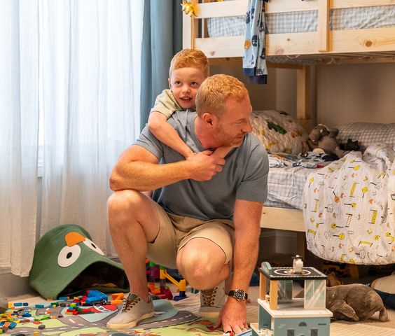 Father and young son playing together in a colorful, toy-filled bedroom with bunk beds.