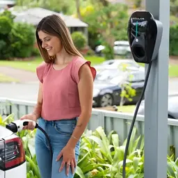 A woman plugging an EV into a home wall charger in her driveway
