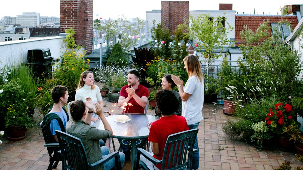 Residents sharing a meal around a table on their building's planted rooftop terrace