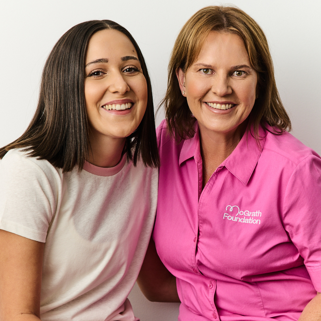 Two people smiling at the camera, one wearing a pink McGrath Foundation shirt.
