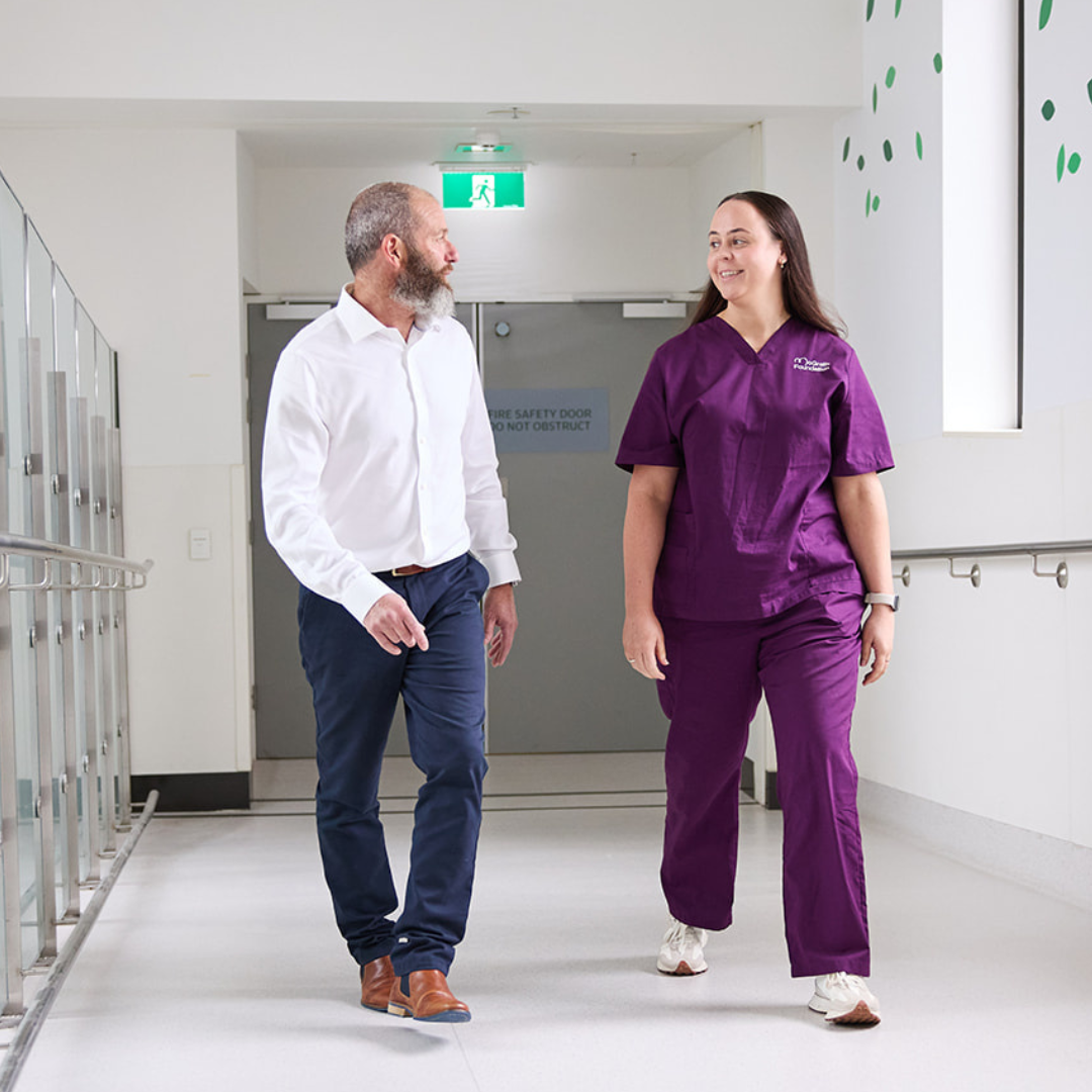Male patient and his McGrath Cancer Care Nurse walking together down the hallway of a health care facility talking to each other