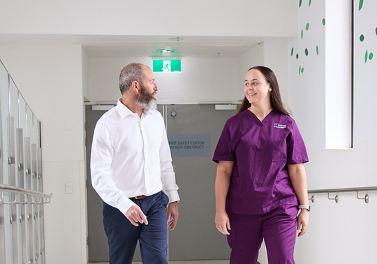 Male patient and his McGrath Cancer Care Nurse walking together down the hallway of a health care facility talking to each other