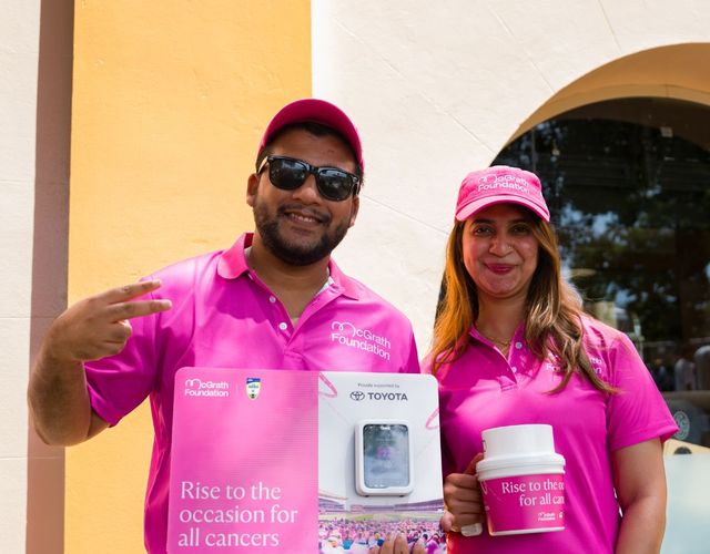 Two McGrath Foundation volunteers hold fundraising materials and a donation collection bucket during a community fundraising event