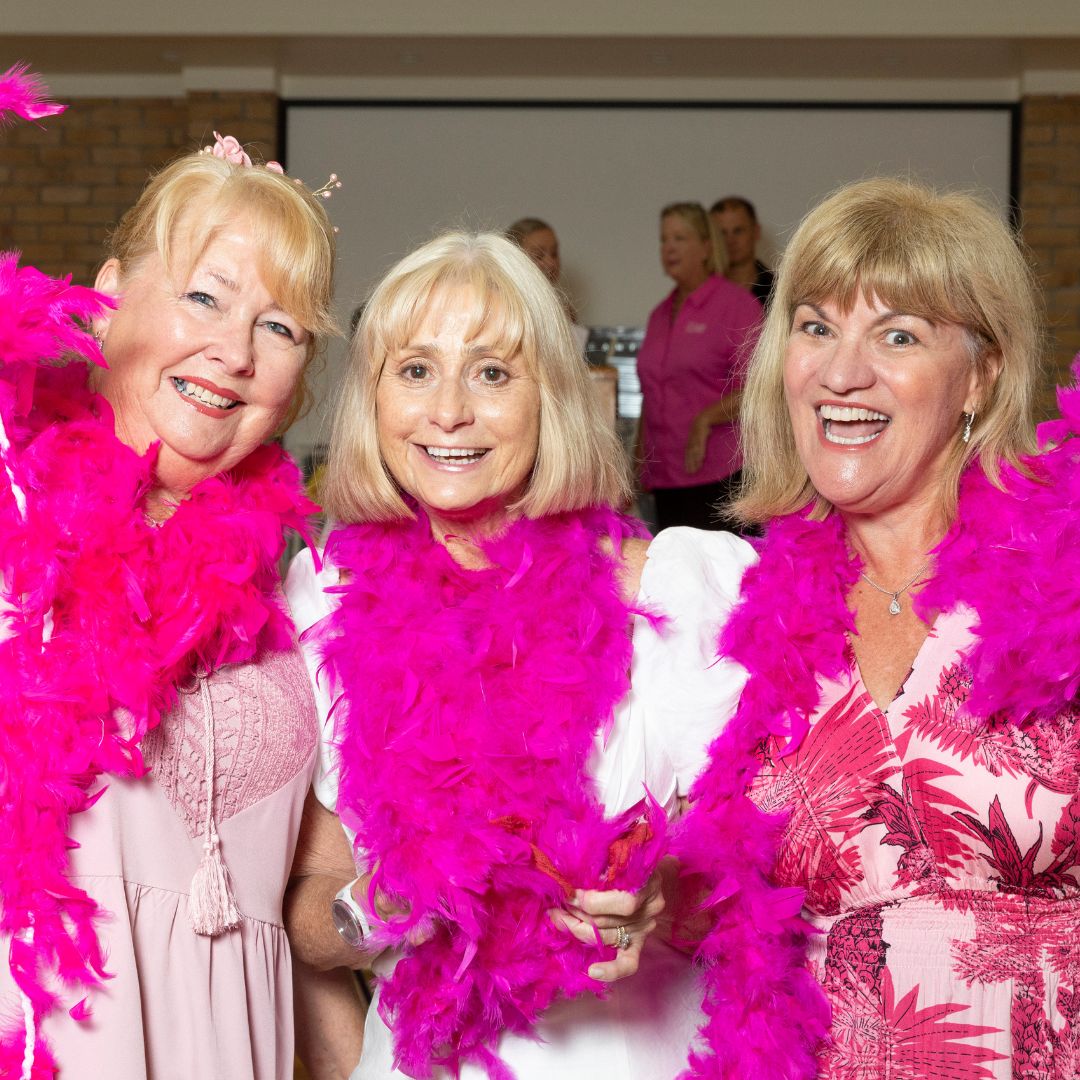 Three community fundraisers at an event wearing bright pink feather bowers