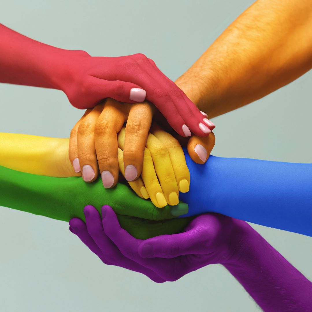 Multiple hands painted in rainbow colours stacked together, symbolising inclusion, support and diversity in cancer care.