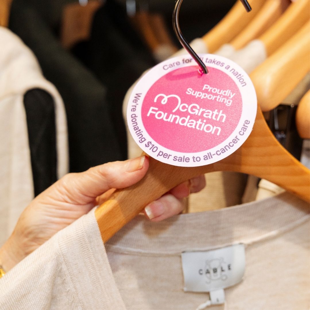 Close-up of a clothing hanger with a tag showing support for the McGrath Foundation and a $10 donation per sale.