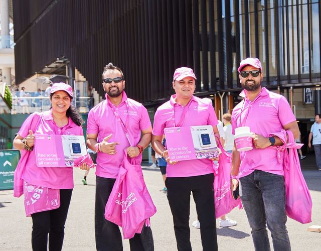 Four McGrath Foundation volunteers stand outdoors with fundraising materials, donation collection buckets and event merchandise