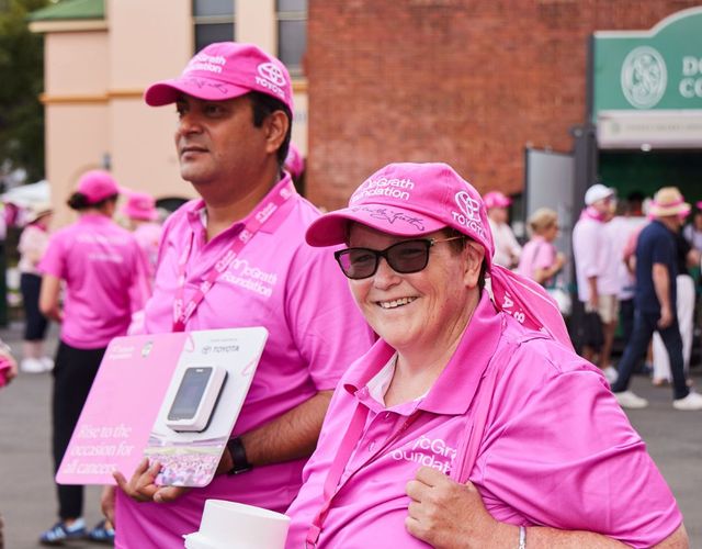 McGrath Foundation volunteers in pink shirts carry donation collection buckets and fundraising materials among participants at a community event