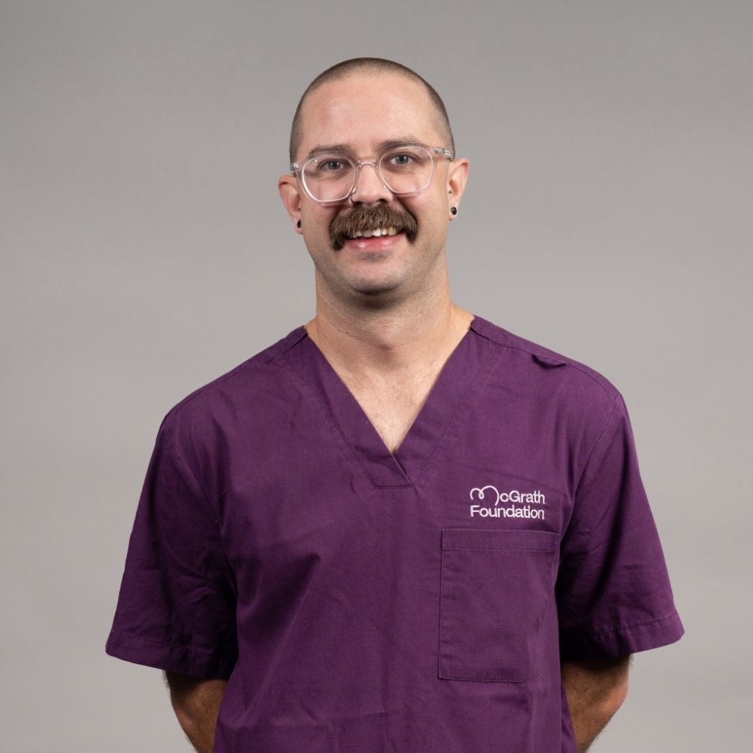 Portrait of a person wearing purple McGrath Foundation scrubs and glasses.
