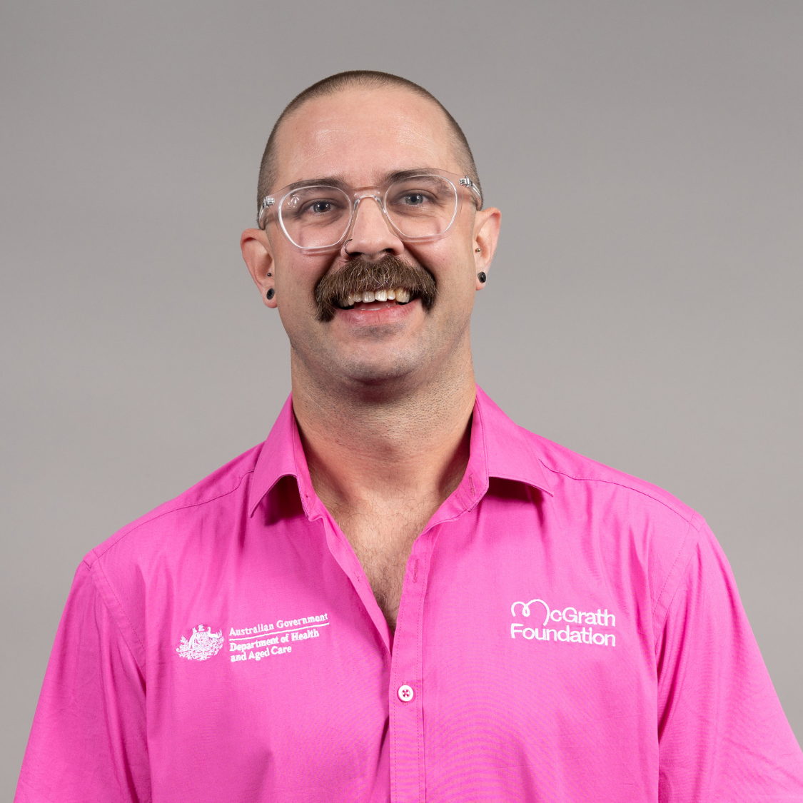 Professional headshot of Daniel Pym wearing a bright pink McGrath Foundation shirt