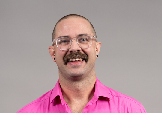 Professional headshot of Daniel Pym wearing a bright pink McGrath Foundation shirt