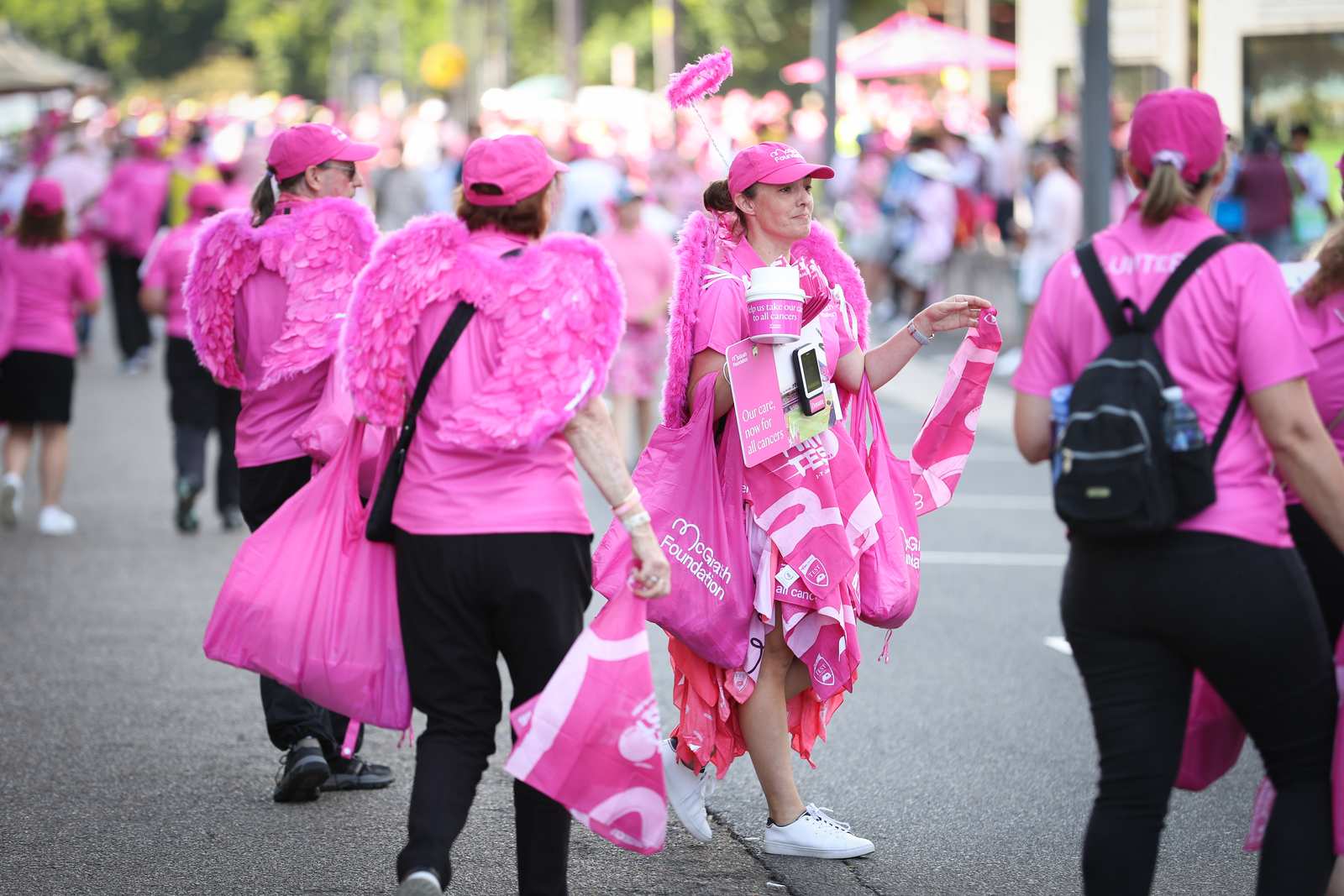 Volunteers in pink walk along a street carrying bags and fundraising materials at the Pink Test..